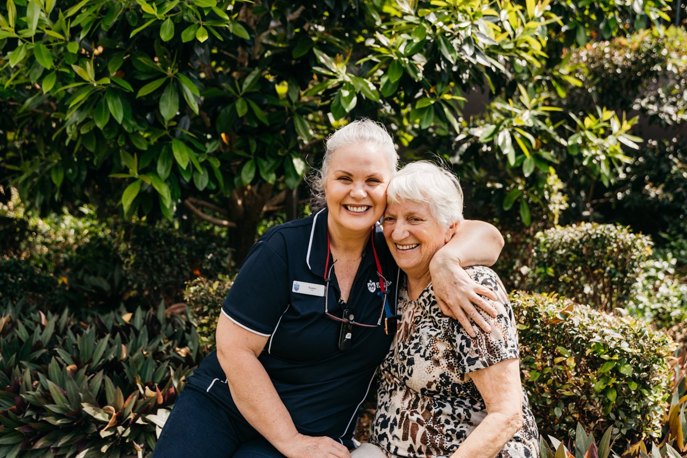 an aged care staff member hugging a resident on a park bench